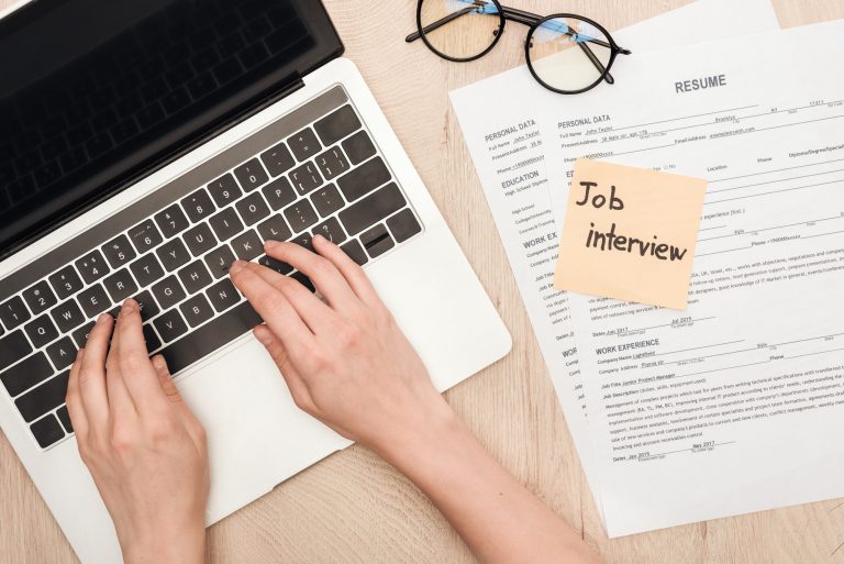 cropped view of recruiter typing on laptop keyboard near glasses, resume templates and sticky note